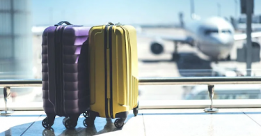purple and yellow suitcase next to each other in an airport with an airplane in the background